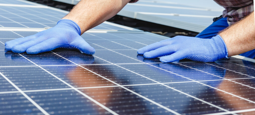 Male worker hands in glows on solar panels, technician installing solar panels on roof. Alternative energy sun energy power, ecological concept. Long web banner