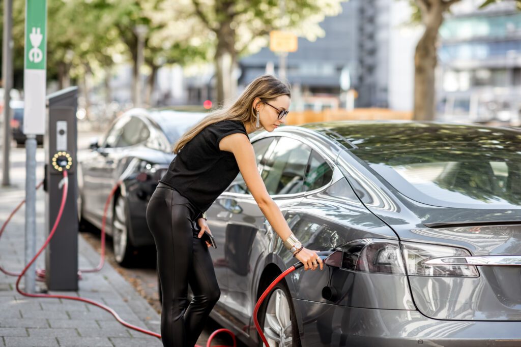 a woman in black clothes plugging an electric vehicle in to charge it benefitting from the ZEV mandate. ev charger.