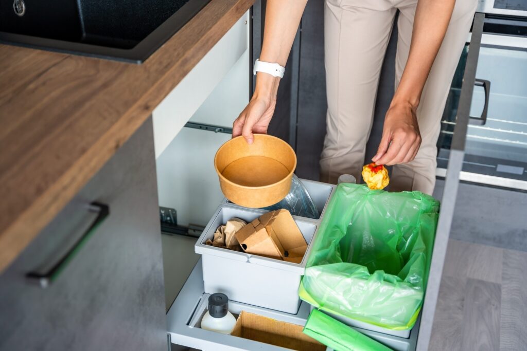 Woman throwing trash into household bins for waste sorting in the kitchen for simpler recycling legislation.